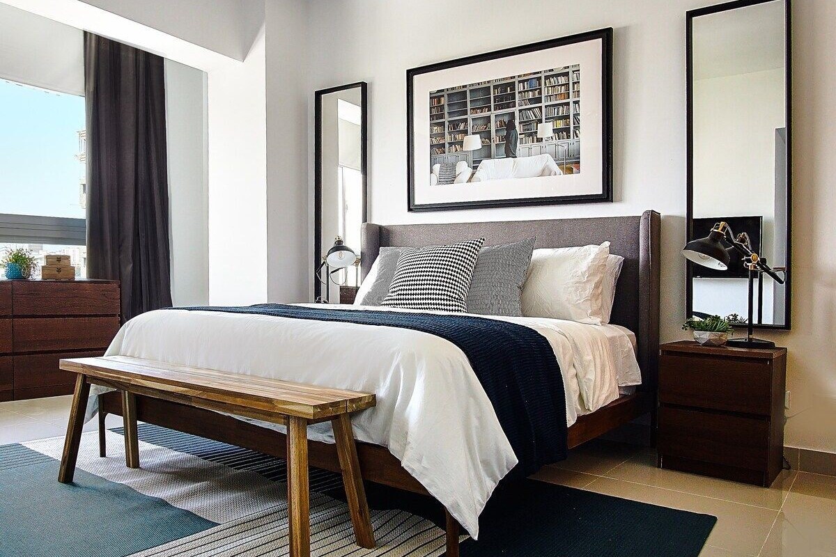 A modern bedroom with a large bed, bedside tables, a bench, and a large window.