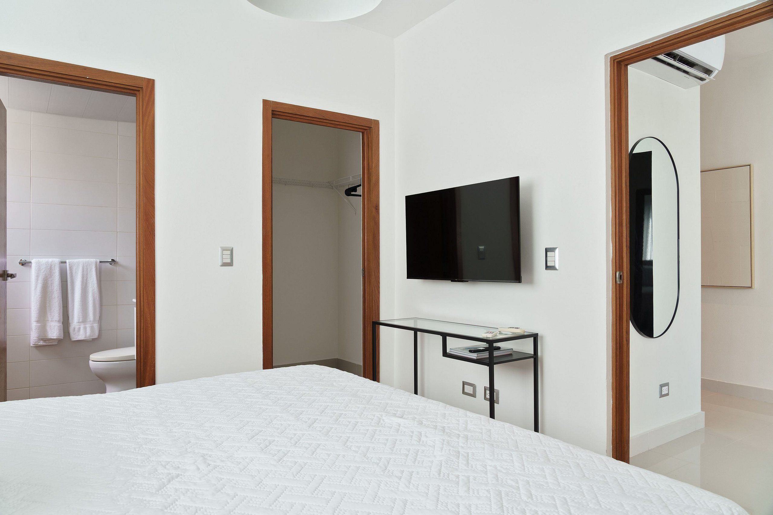 A modern bedroom with a large bed, a mounted TV, a small table, and a mirror.