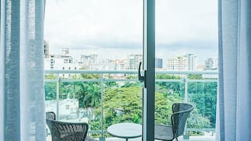 Un balcon avec deux fauteuils en osier et une petite table ronde, d’où l’on peut admirer un paysage urbain composé d’immeubles et d’espaces verts.