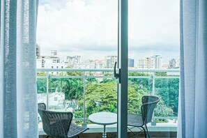 A balcony with two wicker chairs and a small round table, overlooking a cityscape with buildings and greenery. - Torre Armonia 24 (Santo Domingo)