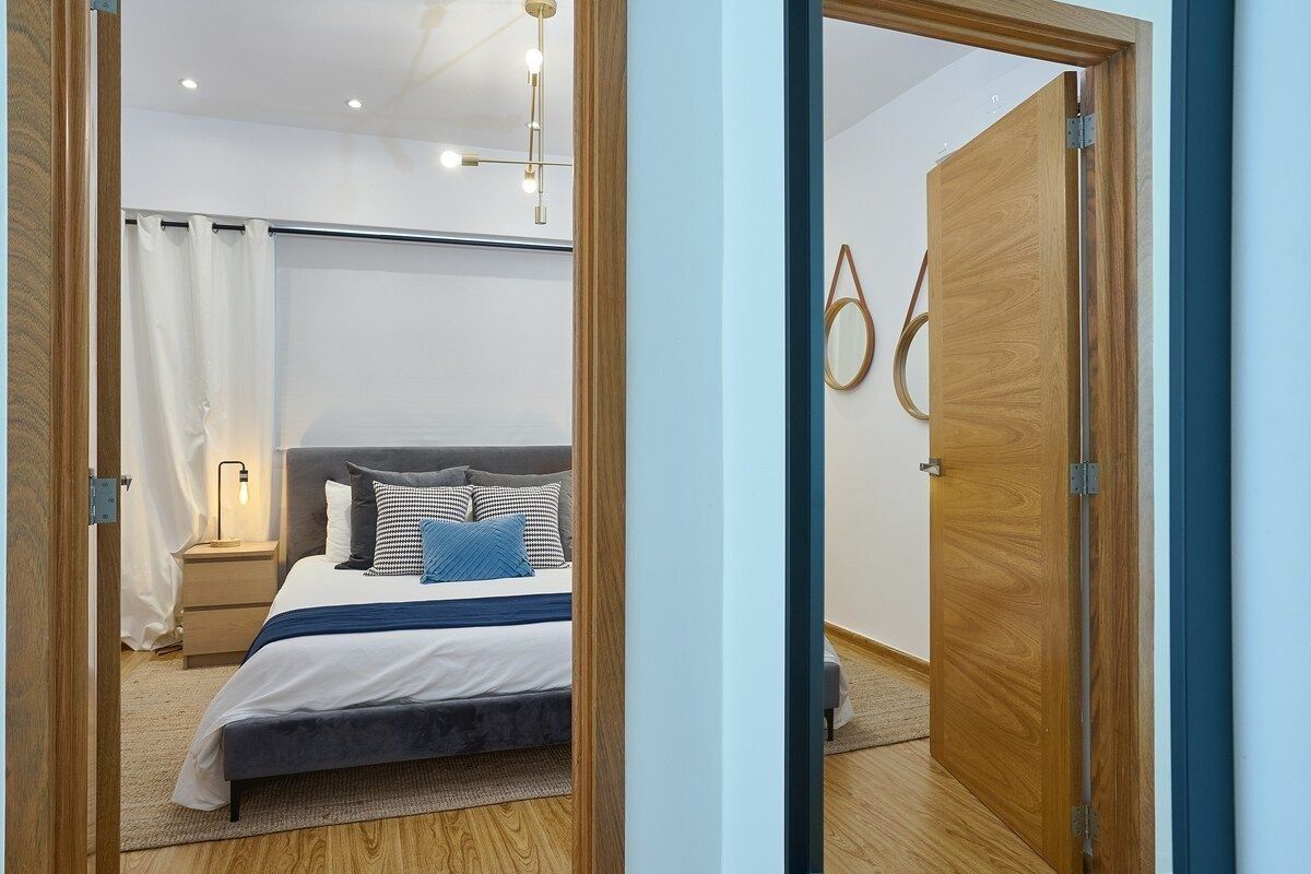 A bedroom with a bed, bedside table, lamp, and a wooden door.