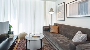 A modern living room with a grey sofa, a glass coffee table, and a large window with sheer curtains. - Torre Armonia 24 (Santo Domingo)