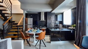 A modern kitchen with a central island, a dining area with a table and chairs, and a staircase with wooden steps and metal railings.