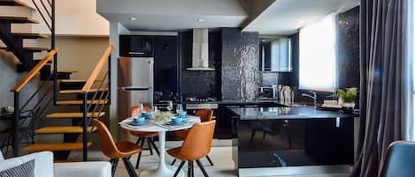 A modern kitchen with a central island, a dining area with a table and chairs, and a staircase with wooden steps and metal railings.