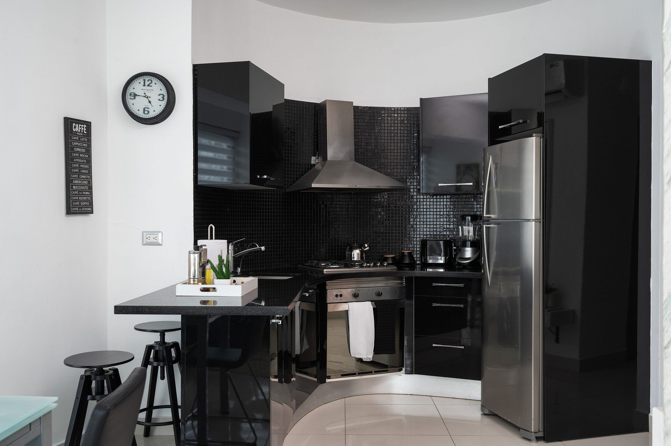 A modern kitchen with a black countertop, stainless steel appliances, and a wall clock.