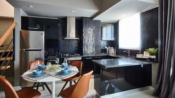 A modern kitchen with a central island, black backsplash, stainless steel appliances, and a dining area with brown chairs and a white table.