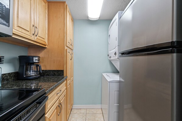 A compact kitchen with wooden cabinets, a stainless steel refrigerator, a coffee maker, and a microwave.