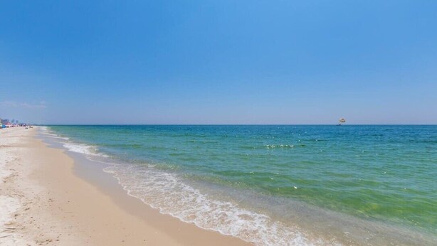 A beach with clear blue water, a sandy shore, and a distant boat.