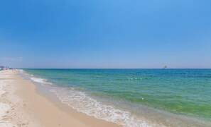 A beach with clear blue water, a sandy shore, and a distant boat.