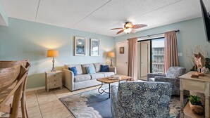 A living room with a sofa, armchairs, a coffee table, and a ceiling fan.
