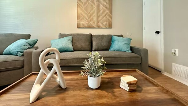 A living room with a grey sofa, teal cushions, a wooden coffee table, a white plant, and a geometric wall art piece. - Chic 2-bedroom apartment with WiFi, AC in enchanting Arlington (Arlington)