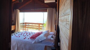 A wooden cabin bedroom with a bed, a nightstand, and a view of the outdoors. - Chale da Montanha (Santo Amaro da Imperatriz)