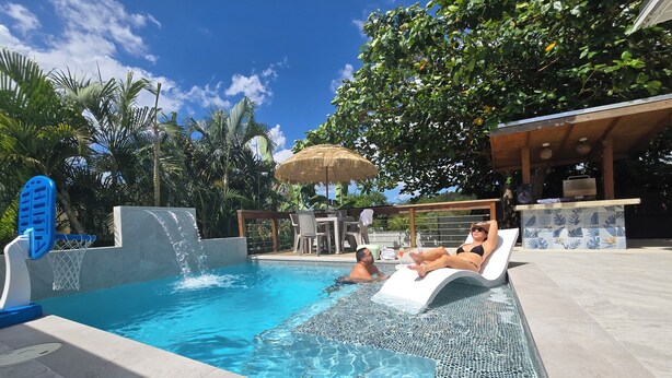 Une piscine avec un toboggan, des chaises longues et un espace bar.