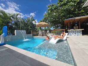 A swimming pool with a water slide, lounge chairs, and a bar area. - Casita Almendro: A Cozy Studio with Heated Pool, BBQ and Close to La Parguera! (San Germán)