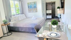 Amplia sala de estar con sofá, mesa de comedor con sillas, zona de cocina y un ventanal con cortinas.