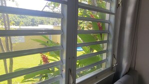 Une pièce dotée d’une fenêtre avec des stores horizontaux, d’un canapé gris et offrant une vue sur la verdure à l’extérieur.