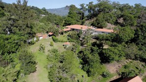 Una casa grande rodeada de abundante vegetación y colinas.