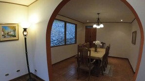 Comedor con una mesa redonda, sillas, una araña y ventana con vistas a rocas.