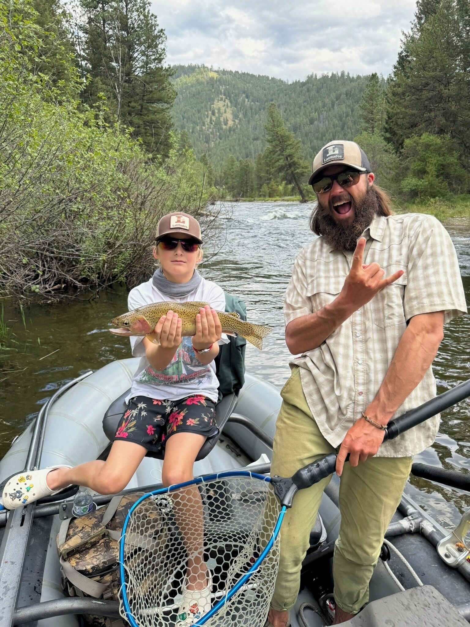 A man and a child on a boat holding a fish, with a net and fishing rod visible.