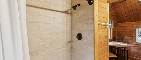 A wooden cabin with a shower area, a sink, and a dining table.
