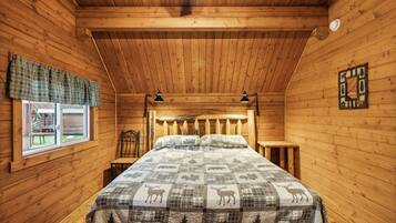 A wooden cabin bedroom with a bed, two nightstands, a window with plaid curtains, and a wall-mounted decoration.