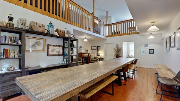 A spacious dining area with a long wooden table, benches, and chairs. There are shelves with books and decorative items, and a staircase leading to an upper level. - Whale's Spout - Pet Friendly-Depoe Bay, OR (Depoe Bay)