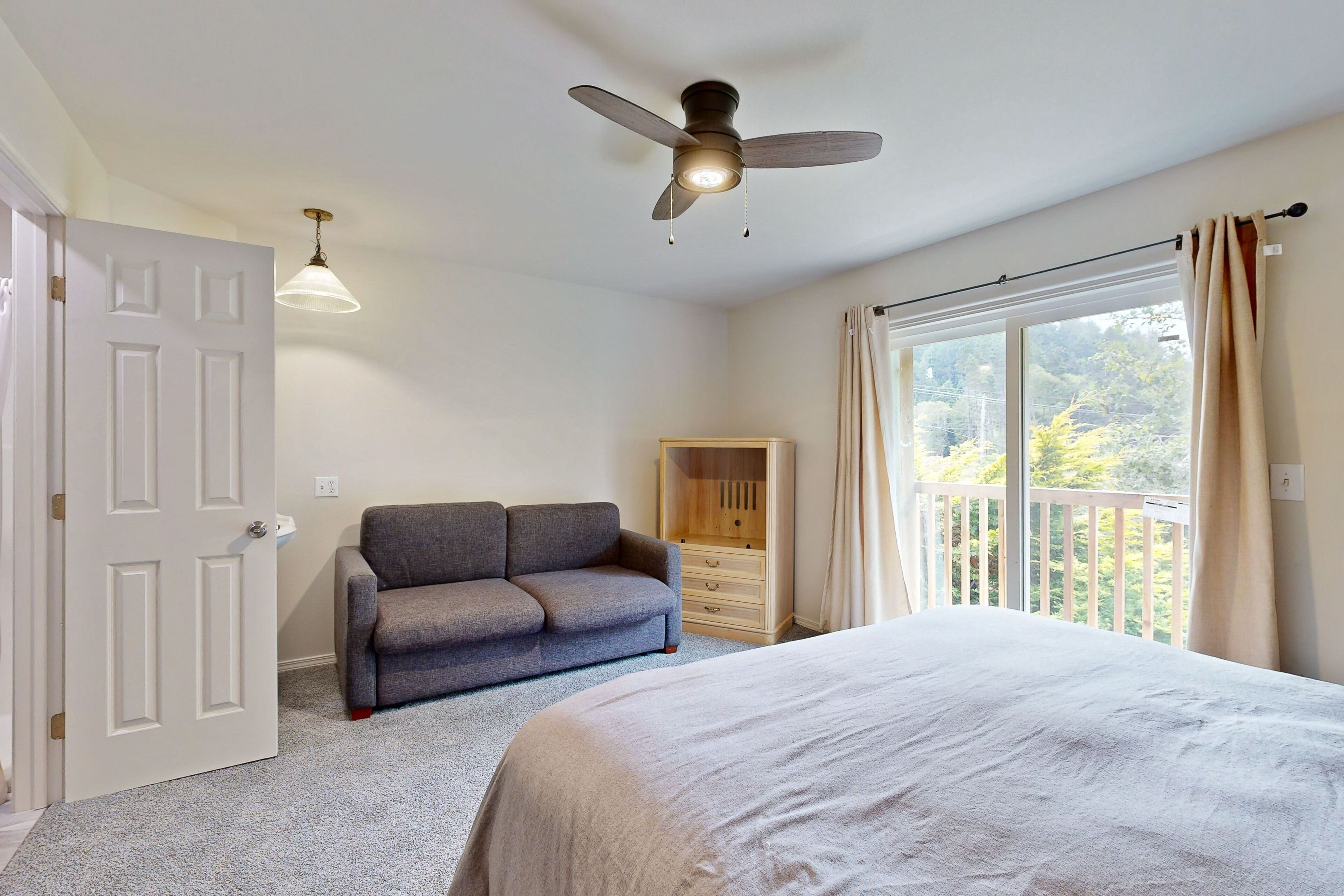 Une chambre à coucher comprenant un lit, un ventilateur de plafond, un canapé, une armoire et une fenêtre avec des rideaux.