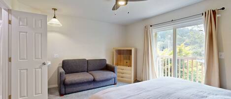 Une chambre à coucher comprenant un lit, un ventilateur de plafond, un canapé, une armoire et une fenêtre avec des rideaux.