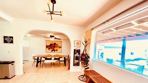 A modern dining area with a large table, chairs, and a ceiling fan. There is a bench along the window and a rug with a geometric pattern on the floor. - Stunning 3-Bed/2-Bath Villa with Hot Tub, Pool, & Garden in Joshua Tree (Joshua Tree)