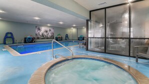 Een binnenzwembad met een jacuzzi, een muurschildering van palmbomen en een glazen ruimte met fitnessapparatuur.