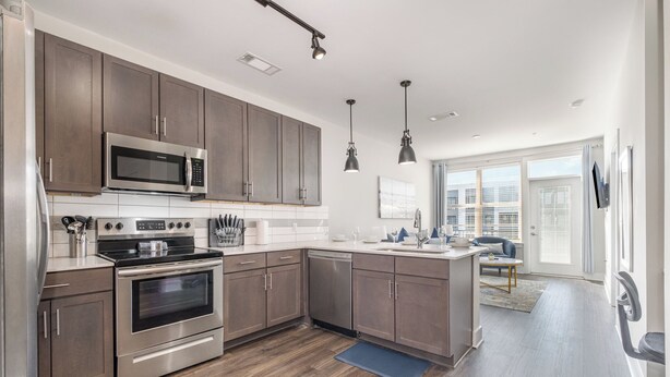A modern kitchen with stainless steel appliances, wooden cabinets, and pendant lighting.