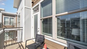 A balcony with a metal railing, a black chair, and a small gnome figurine.