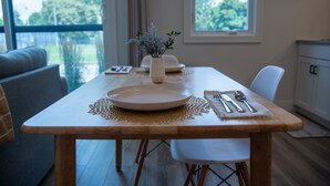 A dining table with a placemat, white plates, cutlery, and a vase with flowers. - Modern Lakeside Escape | Prime Location + Parking (Traverse City)