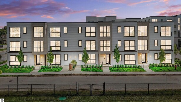 A modern multi-story residential building with large windows and a well-maintained lawn. - Modern Lakeside Escape | Prime Location + Parking (Traverse City)