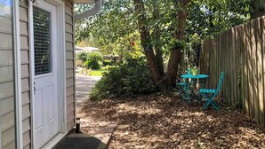 Un jardin à l’arrière d’une maison, avec une clôture en bois, une petite table et des chaises, et un chemin menant à la maison.