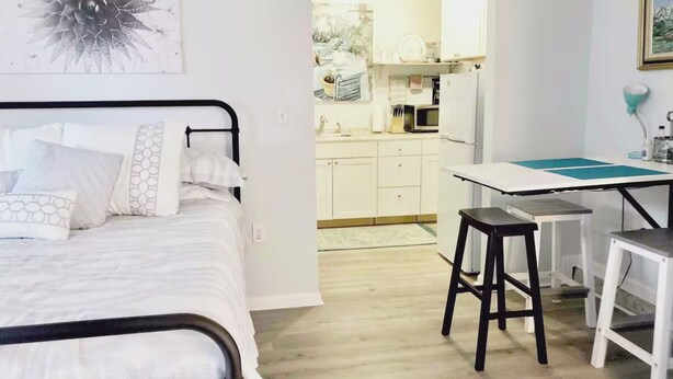 Une chambre avec un lit, un bureau avec une chaise et, au fond, une petite cuisine.