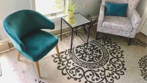 Un fauteuil de couleur turquoise, un fauteuil à motifs, une petite table avec une plante et un tapis décoratif dans une pièce avec une fenêtre.