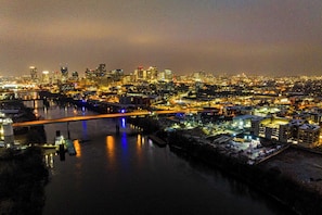 A nighttime cityscape with a river, illuminated buildings, and a bridge. - Cumberland River Views, Walk to Broadway, Downtown & Stadium Rockin' Riverfront (Nashville)
