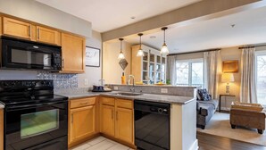 A modern kitchen with wooden cabinets, a black microwave, and a dishwasher. - Cumberland River Views, Walk to Broadway, Downtown & Stadium Rockin' Riverfront (Nashville)