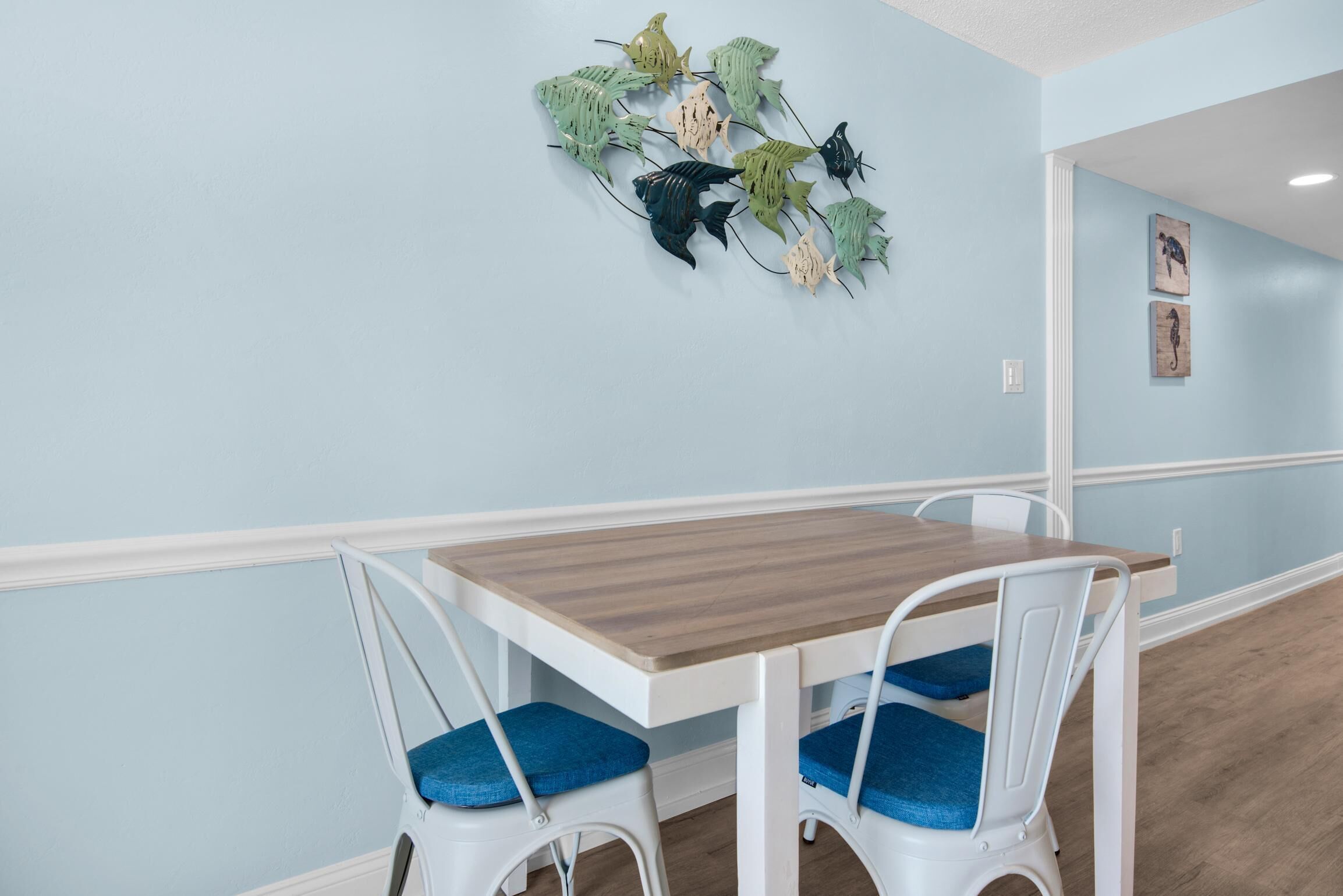 Un coin repas avec une table en bois et des chaises blanches dotées de coussins bleus.