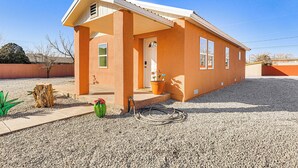 Une maison de plain-pied avec un porche, une porte d’entrée et un petit jardin agrémenté d’un cactus et d’une plante en pot.