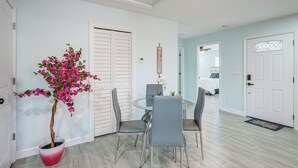 A dining area with a glass table and chairs, a potted plant, and a welcome sign. - Vibrant Tampa Home: Perfect for Long Stays! (Lutz)