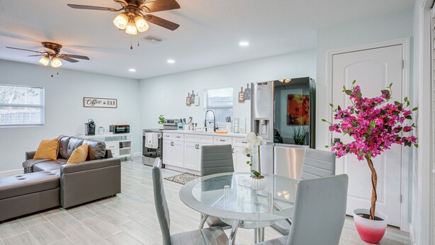A modern kitchen with white cabinets, a dining area with a glass table, and a ceiling fan. - Vibrant Tampa Home: Perfect for Long Stays! (Lutz)