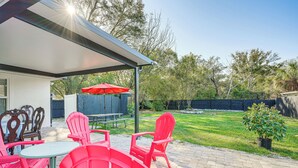 A patio with red chairs and a table, a covered area, and a grassy yard with trees. - Vibrant Tampa Home: Perfect for Long Stays! (Lutz)