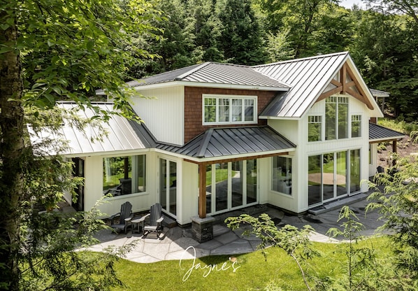 Ein modernes Haus mit großer Glasfront, einer überdachten Terrasse und einem gepflasterten Weg.