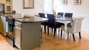 Una cucina moderna con isola centrale, tavolo da pranzo e sedie. Si nota un frigorifero, un forno e degli armadietti.