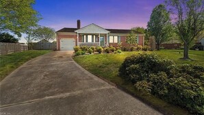 Una casa a due piani in mattoni con un portico, un garage e un prato curato.