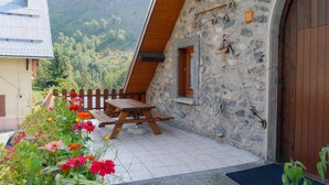 A stone building with a wooden door and window, a wooden bench, and a tiled patio with flowers. - LA GRANGE - 2 VAST CHALET APARTMENTS (70m2) - ALPE D'HUEZ ACCESS (Vaujany)