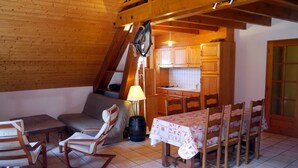 A cozy room with a wooden ceiling, a dining table with chairs, a sofa, and a kitchen area with cabinets and a sink. - LA GRANGE - 2 VAST CHALET APARTMENTS (70m2) - ALPE D'HUEZ ACCESS (Vaujany)