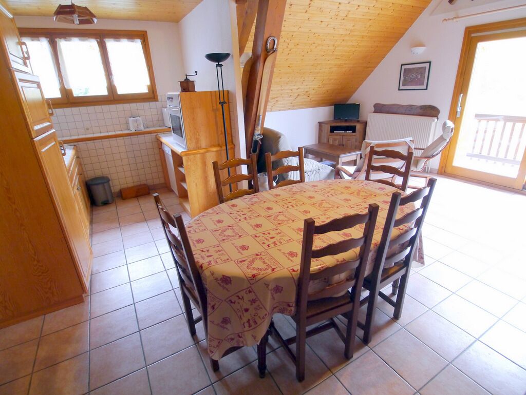 A cozy kitchen with wooden cabinets, a tiled floor, a round table with chairs, and a window providing natural light.